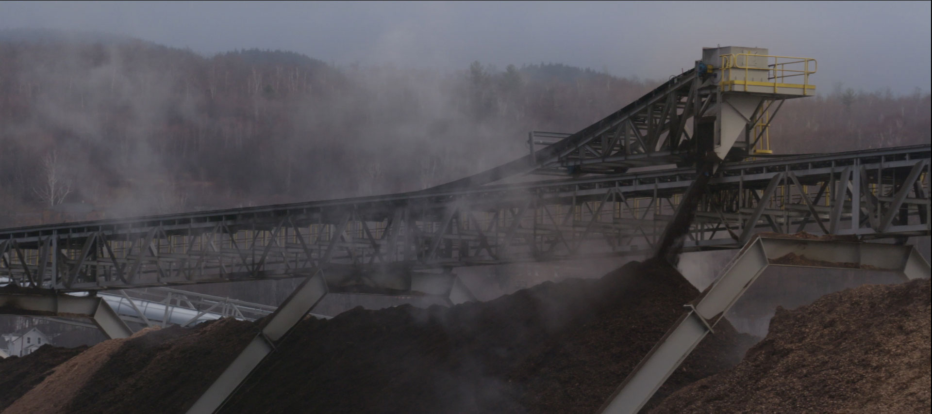 A depressing picture of huge piles of wood chips in an industrial setting with steam coming off them